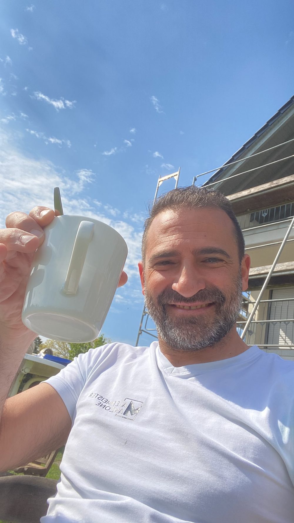 Pietro Manzone lächelt mit einer Tasse Kaffee vor einer Baustelle